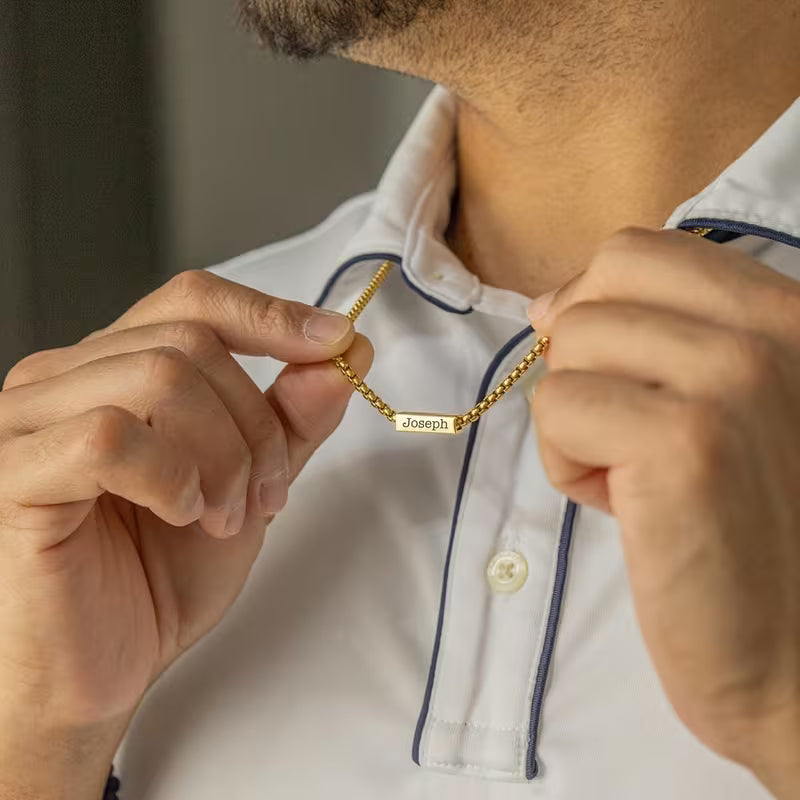 Person adjusting a gold chain necklace with 'Joseph' engraved on it.