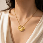 A close-up of a woman wearing a gold necklace with two interlocking circular pendants, one engraved with the name 'ELIZABETH'.